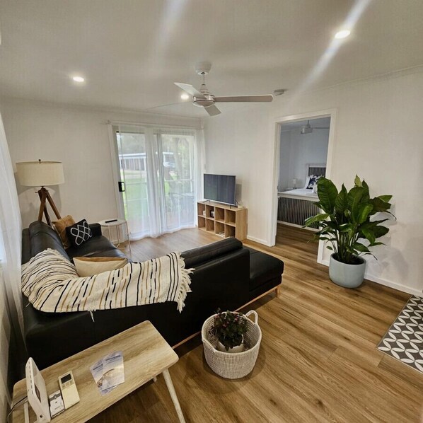 A modern living room with a black sofa, a wooden coffee table, a TV, and a ceiling fan. - Prom Coast - Duneside (Sandy Point)