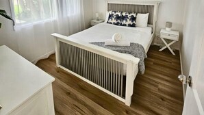 A bedroom with a bed, a bedside table, a nightstand, a ceiling fan, and a window with sheer curtains.