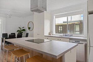 A modern kitchen with a large island, white cabinetry, and a window with a view of the outside. - Prom Coast - Duneside (Sandy Point)