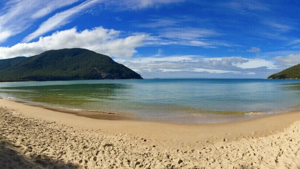 A beach with a clear sky, calm water, and distant mountains.
