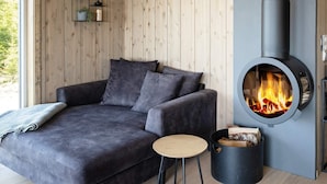 A modern living room with a dark grey sofa, a round wood-burning stove, a small wooden table, and a black trash bin. - 5 Star Holiday Home in Inderoy (Inderøy)