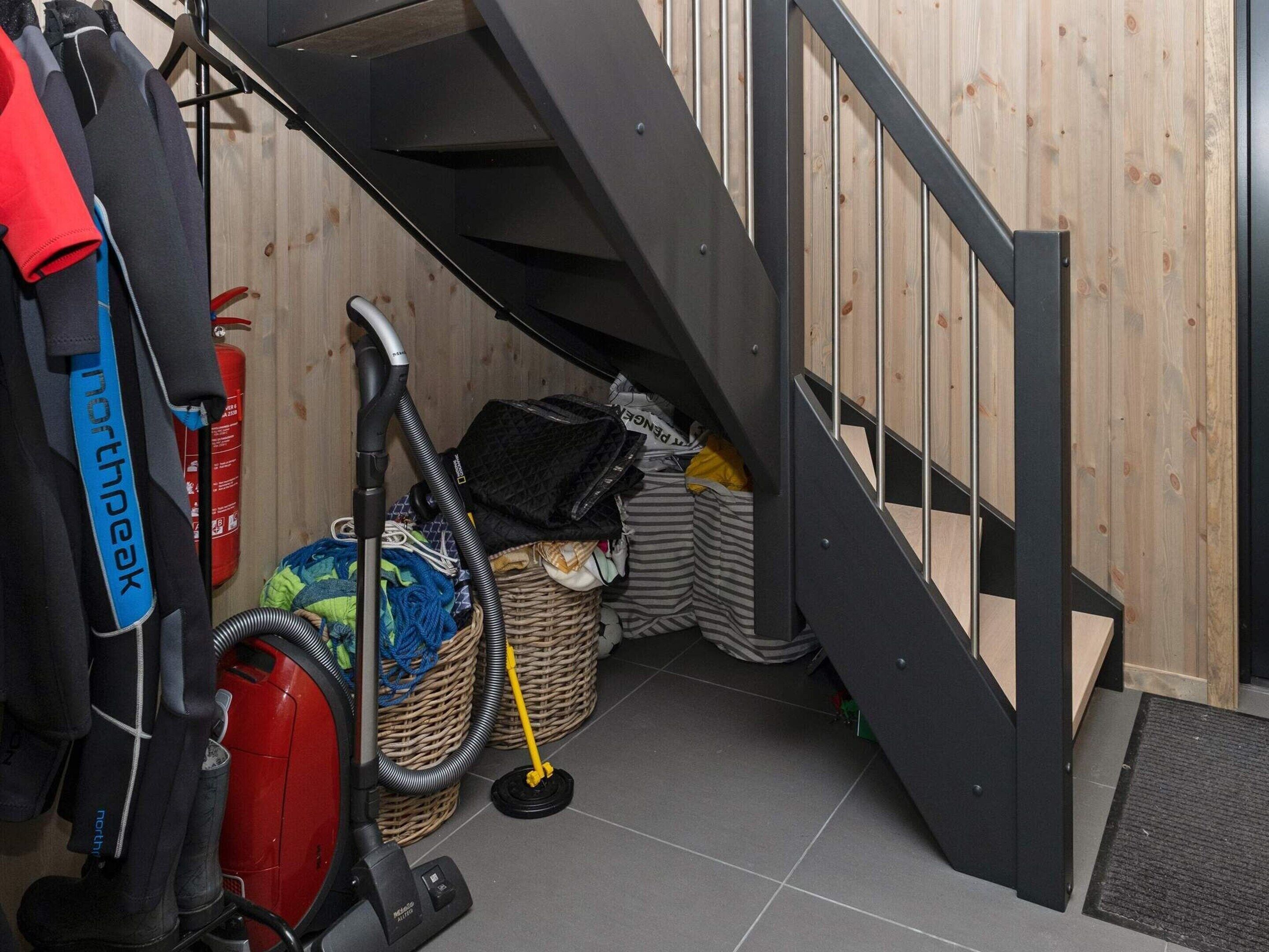 A compact room with a wooden floor, a black staircase, a vacuum cleaner, and a fire extinguisher.