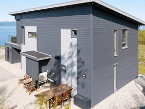 Une maison moderne à deux étages dotée d’un patio comprenant une table et des chaises, un barbecue intégré et une vue sur l’eau.