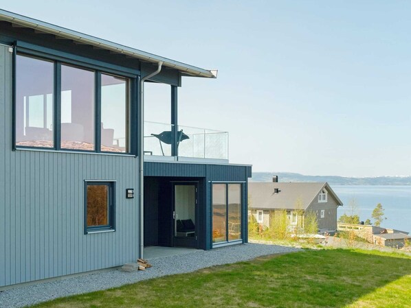 Une maison moderne dotée de grandes fenêtres, d’un balcon et offrant une vue sur l’eau.