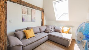 Una sala de estar moderna con un sofá modular, techo de vigas de madera, tragaluz y un ventilador de pie.