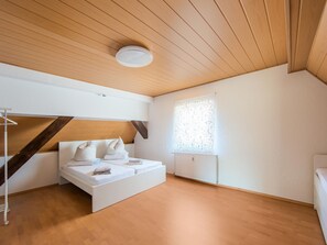 Una camera da letto moderna con soffitto spiovente, un letto con biancheria bianca, un termosifone e una finestra con tende a motivi.
