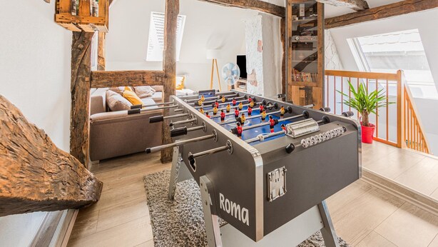 Una habitación acogedora con mesa de fútbol, vigas de madera, un sofá y una escalera.