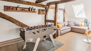 Una habitación acogedora con vigas de madera a la vista, una mesa de fútbol de mesa, un sofá y un ventilador.