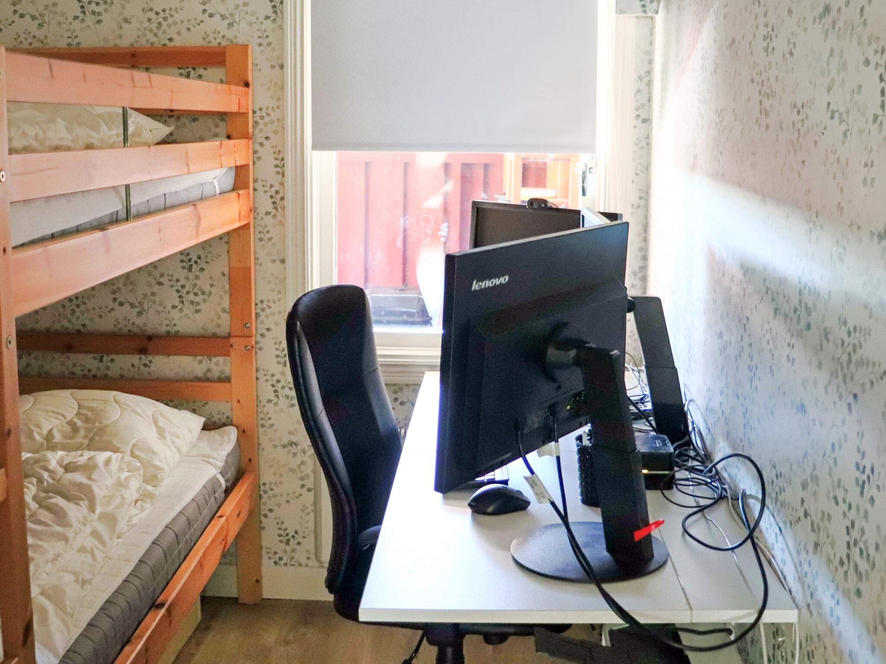 A bunk bed with a desk and a Lenovo computer in a room with floral wallpaper.