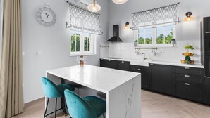 A modern kitchen with a white marble island, two teal bar stools, pendant lights, and a black range hood. - Modern Villa With Swimming Pool and Fenced Garden (Zminj)
