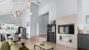 A modern living room with a green sofa, a wooden coffee table, and a fireplace. There is a dining area with a kitchen in the background. - Modern Villa With Swimming Pool and Fenced Garden (Zminj)