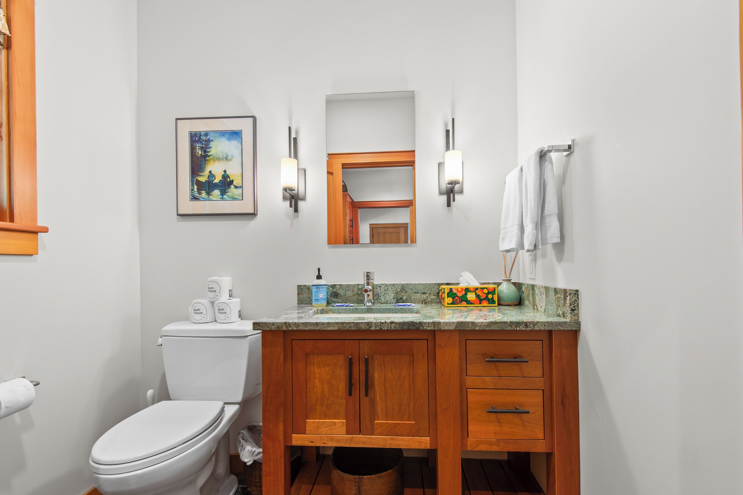 Une salle de bain comprenant des toilettes, un lavabo, des meubles en bois, un miroir et un tableau encadré accroché au mur.