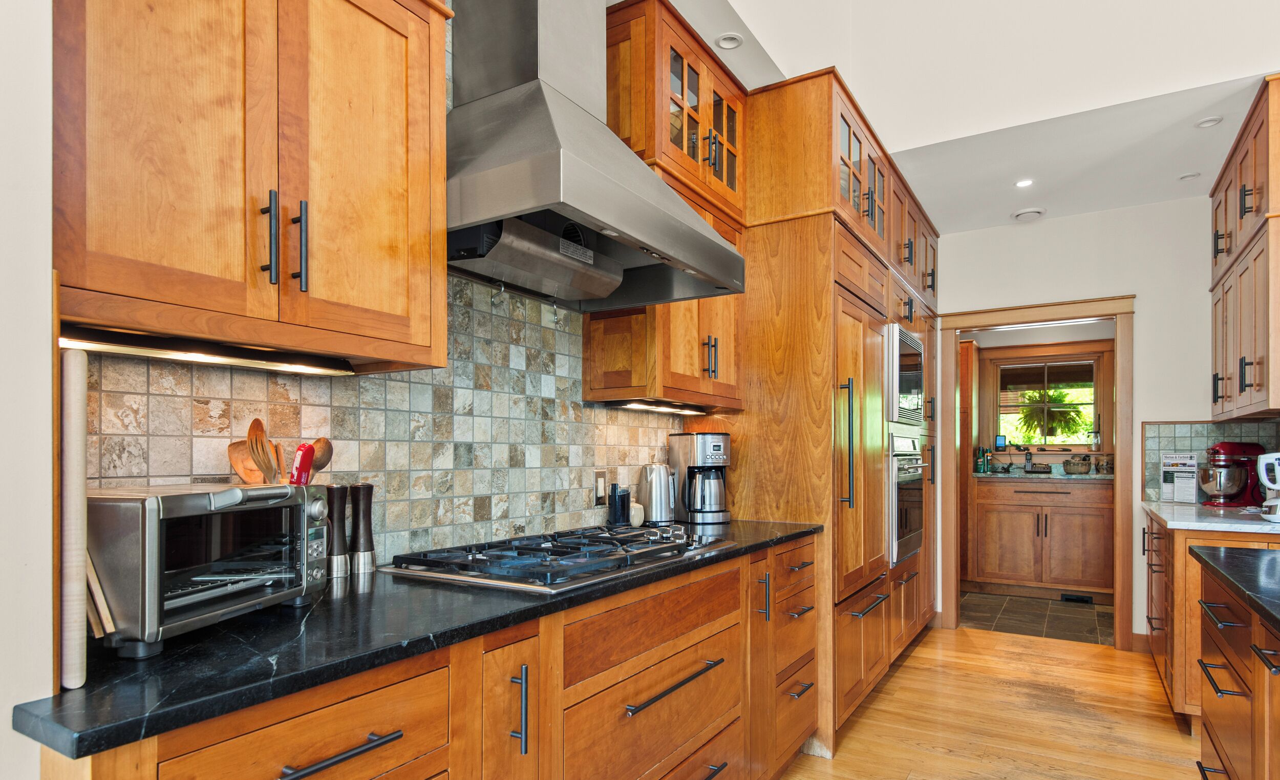 A kitchen with wooden cabinets, a black countertop, and a stone backsplash.