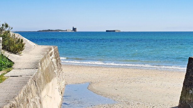Ein Küstenstrand mit einer Betonpromenade und einem kleinen Wasserlauf.
