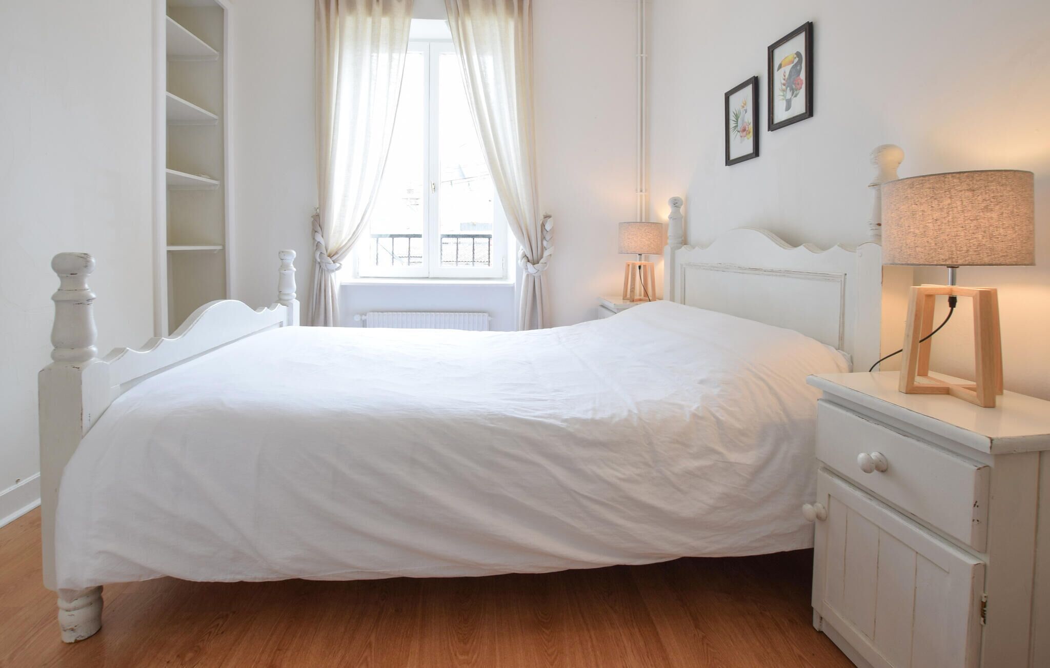 Une chambre à coucher blanche avec un lit, une table de chevet, une lampe et un radiateur.