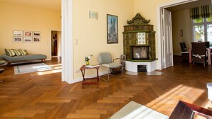 A spacious living room with wooden flooring, a green fireplace, a sofa, and a dining area.