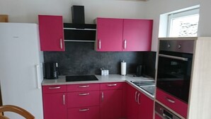 A compact kitchen with pink cabinets, a white refrigerator, a black range hood, and a window with a view. - Rednak Modern Retreat (Polch)