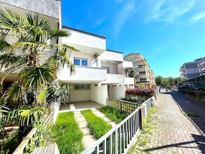 A residential building with balconies, a paved pathway, and lush greenery. - Stylish Villa in Caorle Near Beach (Caorle)
