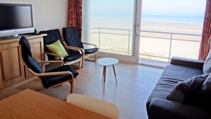 A hotel room with a balcony, a television, two armchairs, a sofa, and a small table.