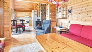 A cozy cabin interior with wooden walls, a stone fireplace, a dining area, and a living room with a red sofa and a wooden table.