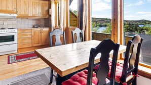 A wooden cabin with a kitchen, dining area, and large windows offering a view of a lake and hills.