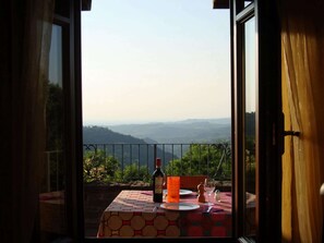 Mesa para dos con una botella y vasos, con vistas a un paisaje montañoso.