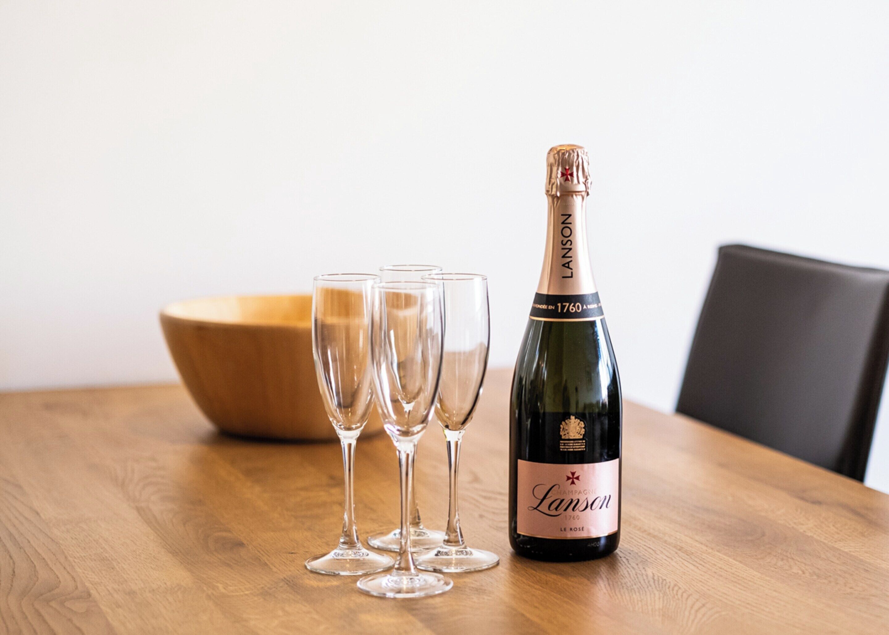 A bottle of champagne and three glasses on a wooden table.