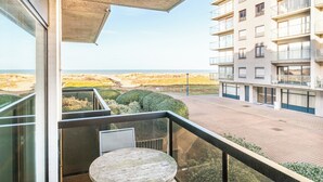 A balcony with a table and chairs, overlooking a beach and a building with multiple balconies. - Family Stay in Oostduinkerke (Koksijde)