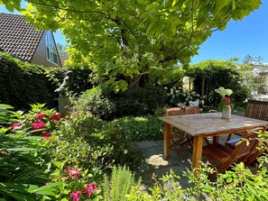 A wooden table and chairs set outdoors in a garden with various plants and flowers. - Holiday Home Near Noordwijk Beach (Noordwijkerhout)