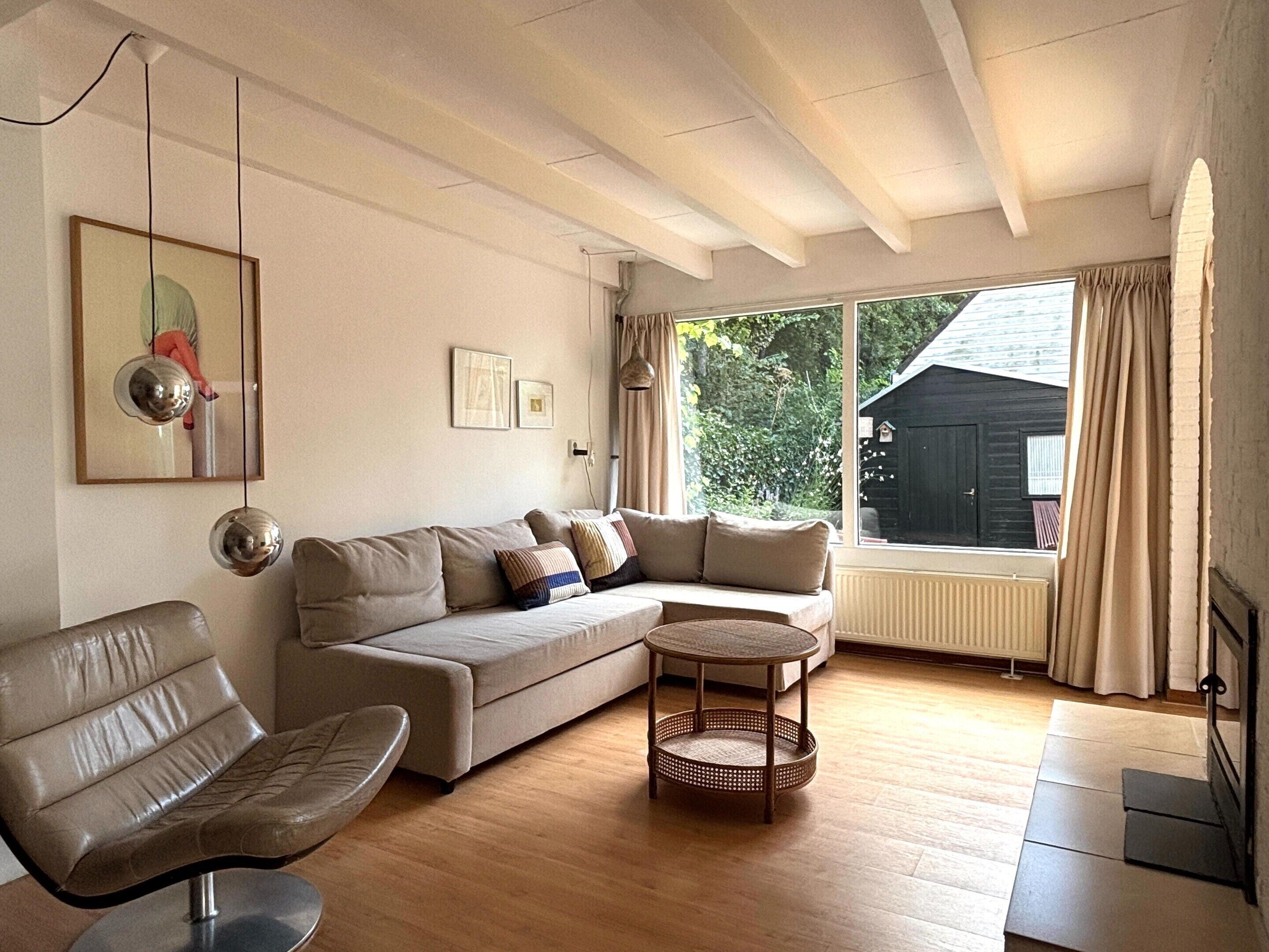 A living room with a sofa, a chair, a small table, and a large window with curtains.