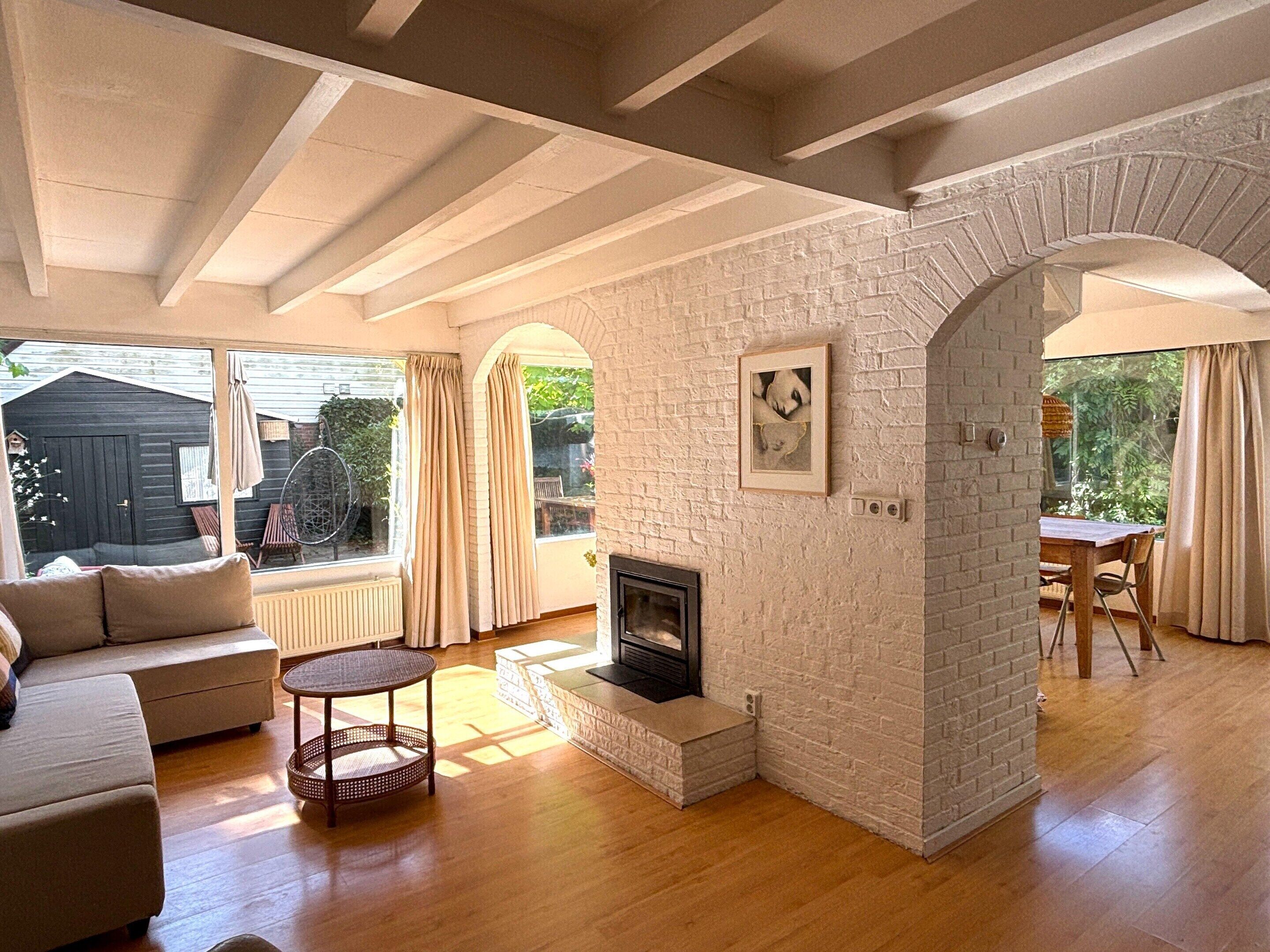 A living room with a fireplace, wooden flooring, a sofa, and a dining area with a table and chairs.