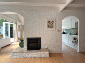 A modern living room with a fireplace, white brick walls, and a kitchen area with white cabinets.
