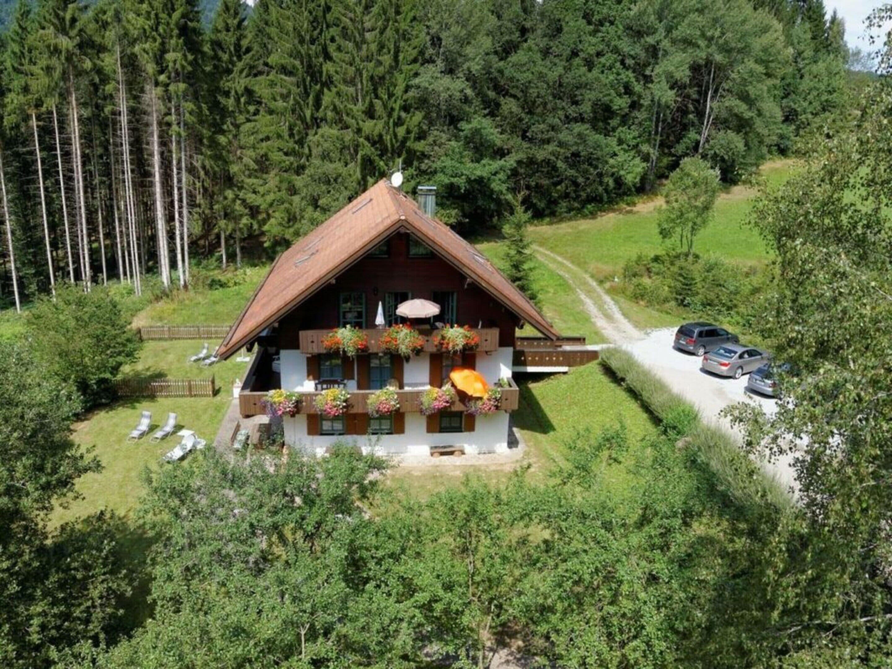 Ein Chalet mit geneigtem Dach, einem Holzbalkon mit Blumenkästen und einer gepflasterten Auffahrt mit parkenden Autos.