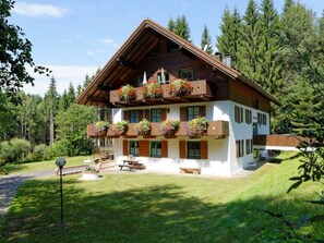A two-story wooden chalet with balconies adorned with flower boxes, a patio area with benches, and a lush green landscape. - Waldhaus Sonnenberg Apartment 2 (Drachselsried)