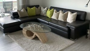 A modern living room with a black leather sofa, a glass coffee table, and a light-colored rug. - Holiday Apartment Casa Chimp 6 (Gambarogno)