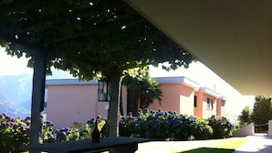 An outdoor patio area with a picnic table, a pergola, and a building with a peach-colored facade. - Holiday Apartment Casa Chimp 6 (Gambarogno)