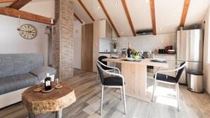 A modern kitchen with a central island, wooden beams, a stone pillar, and a dining area with two chairs. - Apartments Bella Vista - One Bedroom Apartment With Sea View (Kastav)