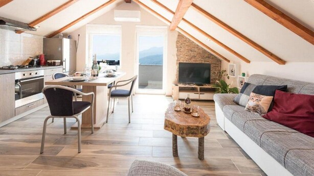 A spacious loft with a kitchen, dining area, and living room, featuring exposed wooden beams, a stone wall, and a large TV. - Apartments Bella Vista - One Bedroom Apartment With Sea View (Kastav)