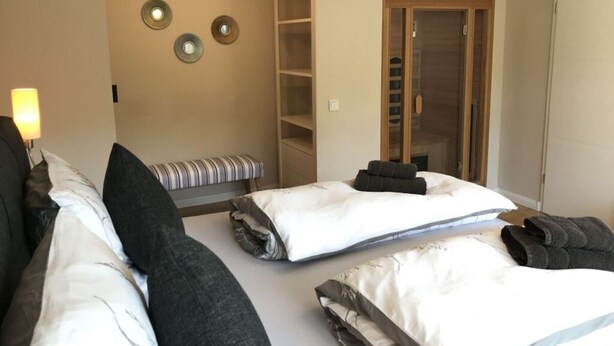 A hotel room with two beds, a bench, a wardrobe, and a mirror on the wall. - Holiday Apartment Summit Nest (Braunlage)