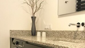 A modern bathroom with a granite countertop, a washing machine, a mirror, and a vase with branches. - Holiday Apartment Summit Nest (Braunlage)