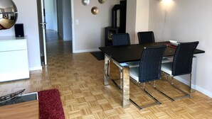 A modern dining area with a black table and chairs, a wooden floor, and a kitchen area visible in the background. - Holiday Apartment Summit Nest (Braunlage)