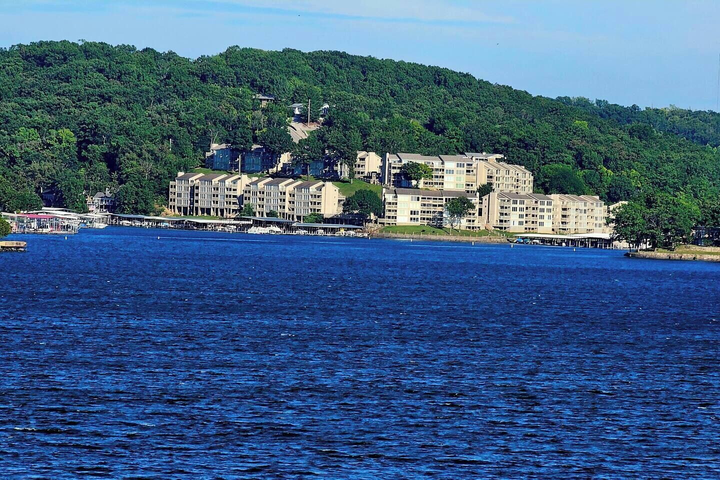 Un hôtel situé au bord de l’eau, composé de plusieurs bâtiments, doté d’une jetée et surplombant une colline boisée.