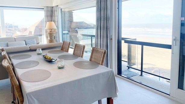 Un espace repas moderne avec une table dressée pour quatre personnes, donnant sur une plage.