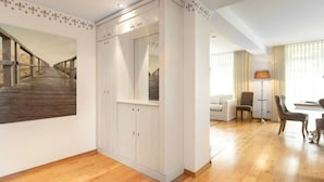 Ein geräumiges Zimmer mit Holzboden, einem weißen Kleiderschrank, einem großen Spiegel, einer Couch, einem Couchtisch und einer Lampe.