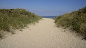 Ein Sandweg am Strand, gesäumt von grasbewachsenen Dünen, der zum Meer führt.