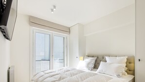 A bedroom with a large bed, a sliding glass door to a balcony, and a mounted TV. - Apartment Next to the Casino (Blankenberge)