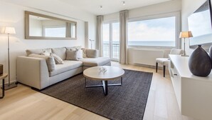 A modern living room with a sofa, a coffee table, and a view of the sea. - Apartment Next to the Casino (Blankenberge)