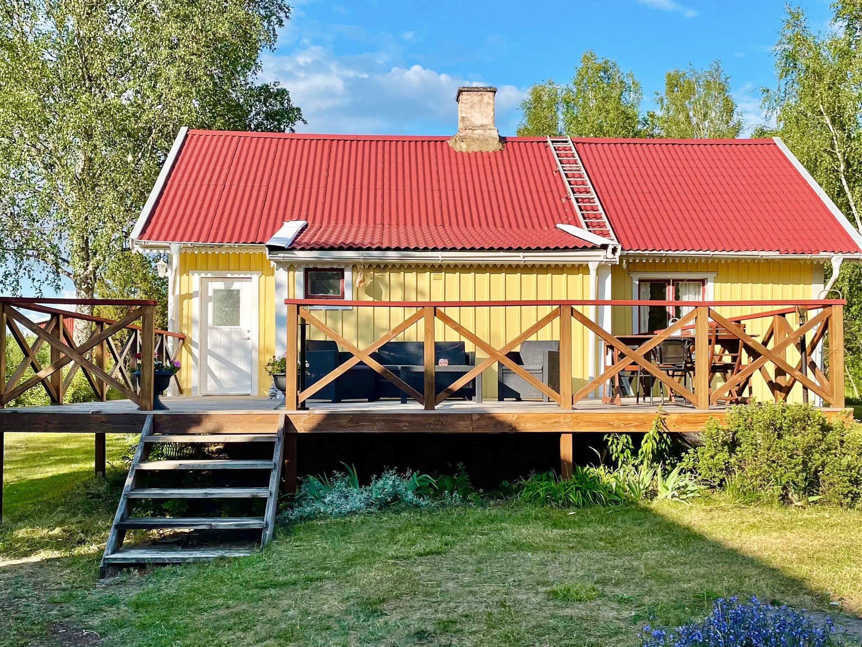 Un bâtiment jaune avec un toit rouge, une terrasse en bois et un escalier menant à l’entrée.