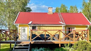 A yellow building with a red roof, a wooden deck, and a staircase leading to the entrance. - 7 Person Holiday Home in Hogsby (Högsby)