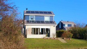 A two-story house with solar panels on the roof, a front porch, and a small garden area. - 158-type 4l1- Strand Park (De Koog)